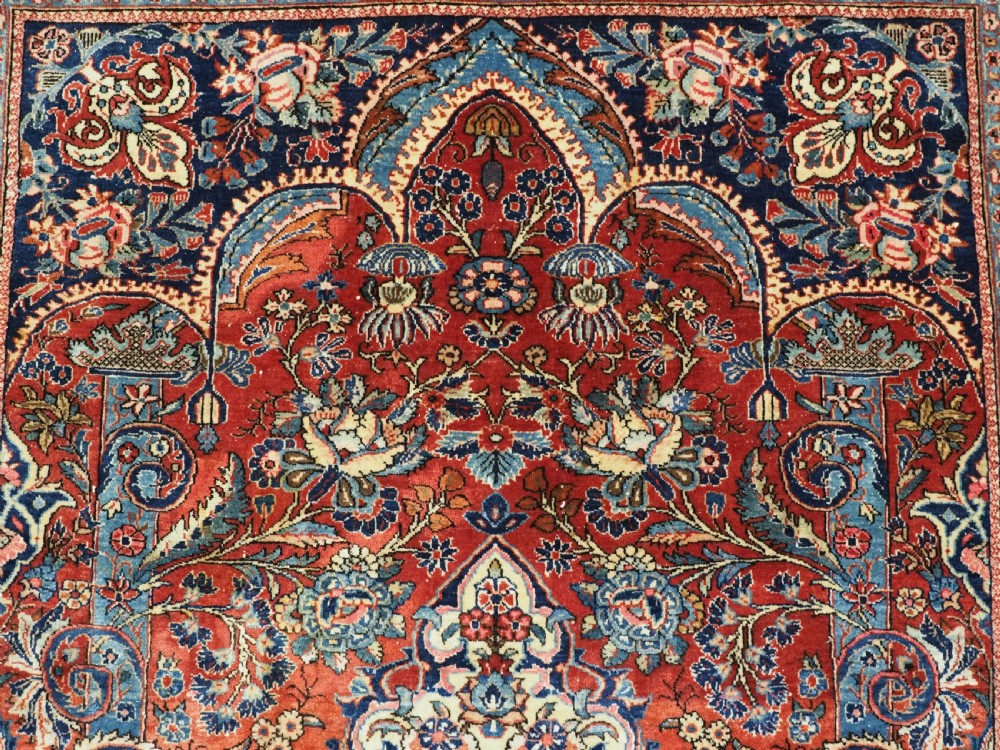 A hand-knotted wool Kashan prayer rug featuring a central floral medallion, a mihrab arch design, and intricate botanical borders in red, navy blue, and cream hues. View IX
