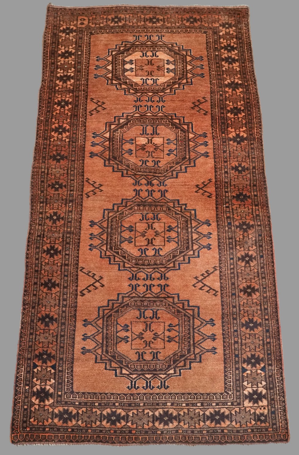 An antique long hand-knotted wool rug featuring four large central turreted octagonal guls on a terracotta field with geometric borders.