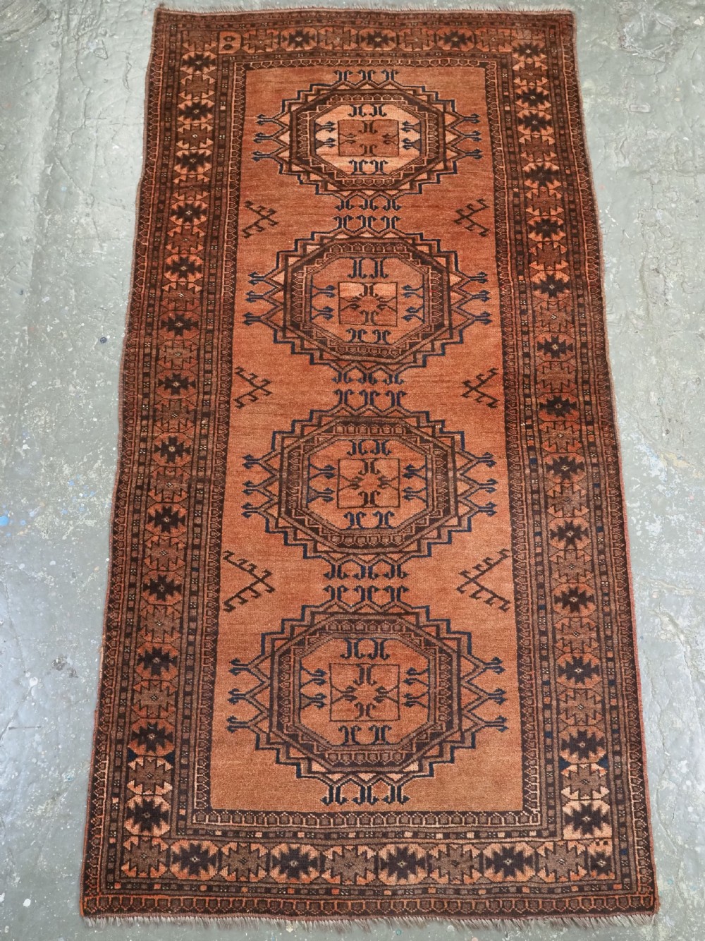 An antique long hand-knotted wool rug featuring four large central turreted octagonal guls on a terracotta field with geometric borders. View II