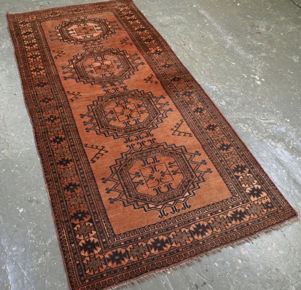 An antique long hand-knotted wool rug featuring four large central turreted octagonal guls on a terracotta field with geometric borders. View III