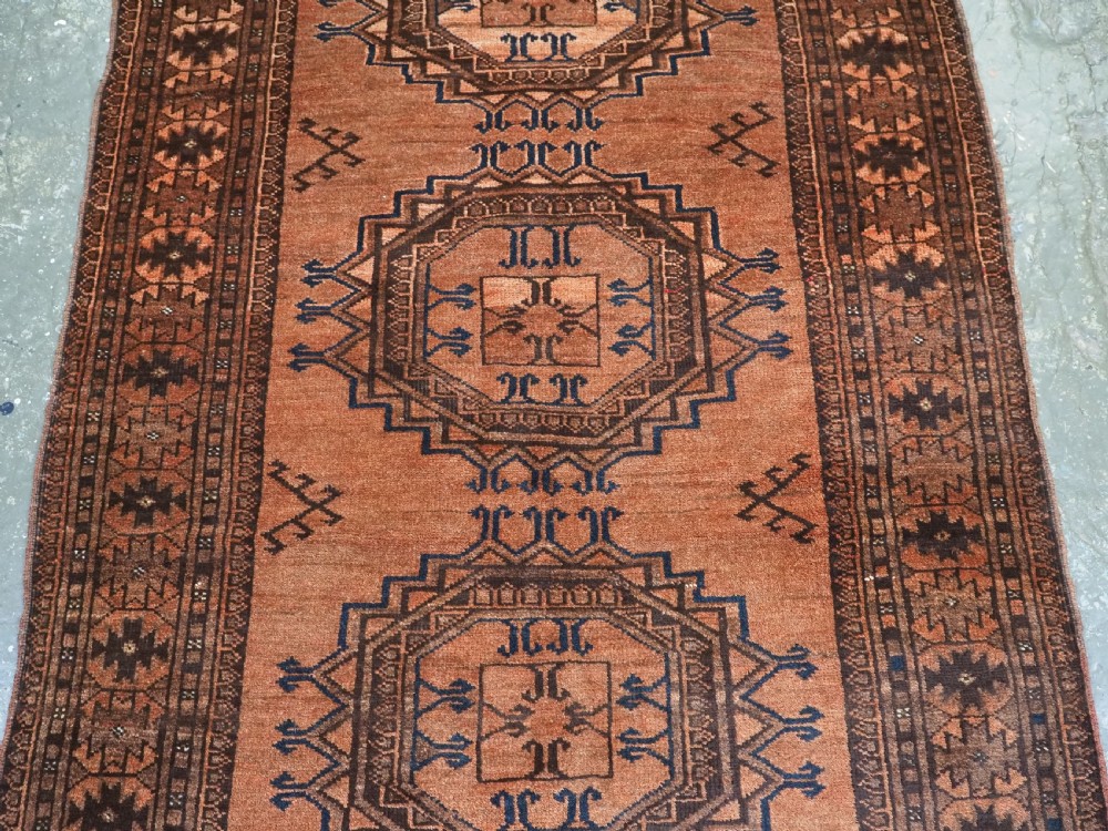 An antique long hand-knotted wool rug featuring four large central turreted octagonal guls on a terracotta field with geometric borders. View IV