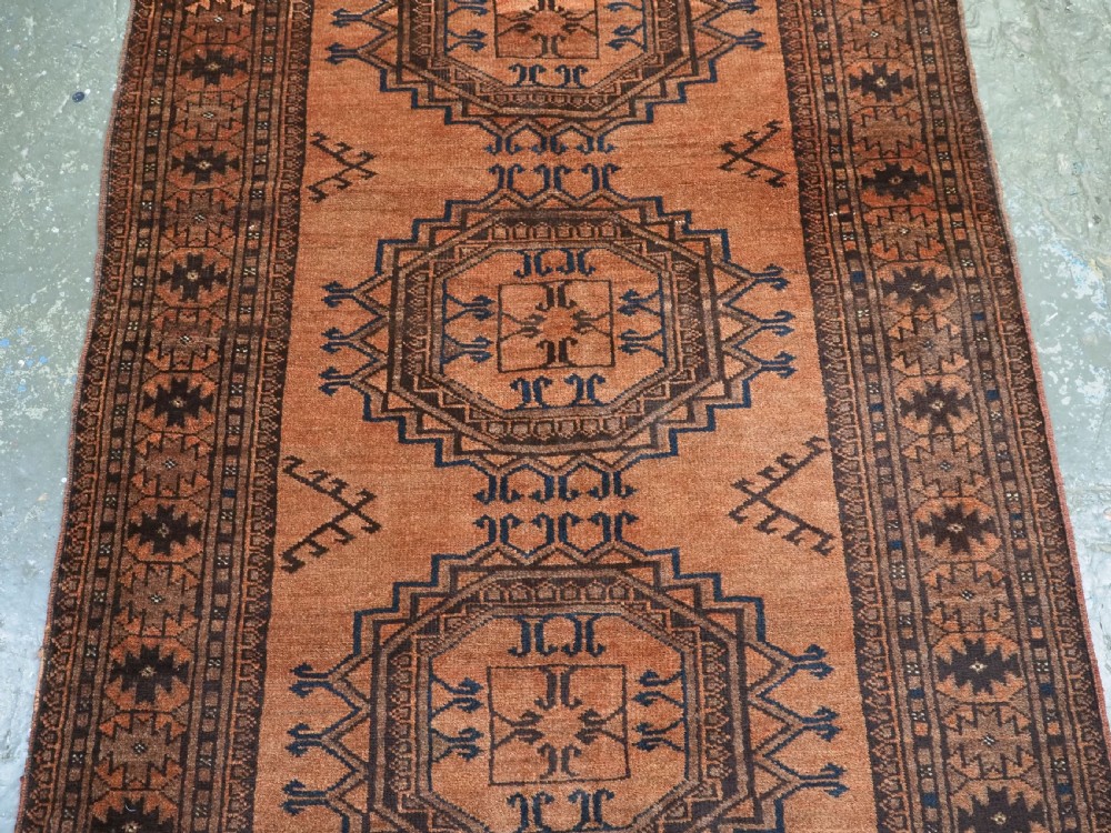 An antique long hand-knotted wool rug featuring four large central turreted octagonal guls on a terracotta field with geometric borders. View V