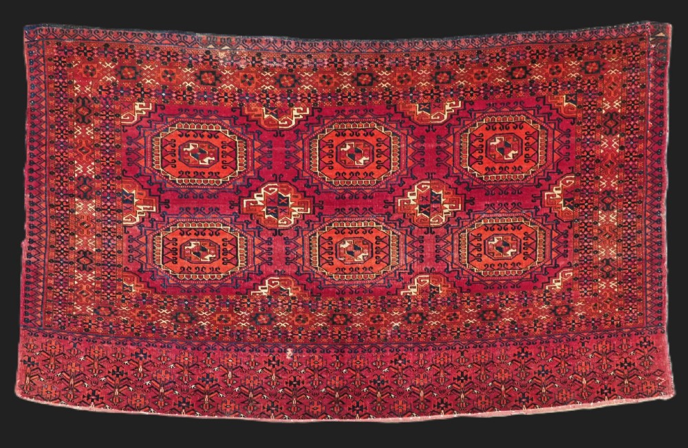 An antique Tekke Turkmen chuval face textile featuring six octagonal turreted guls framed by geometric borders in deep red, navy, and cream wool.