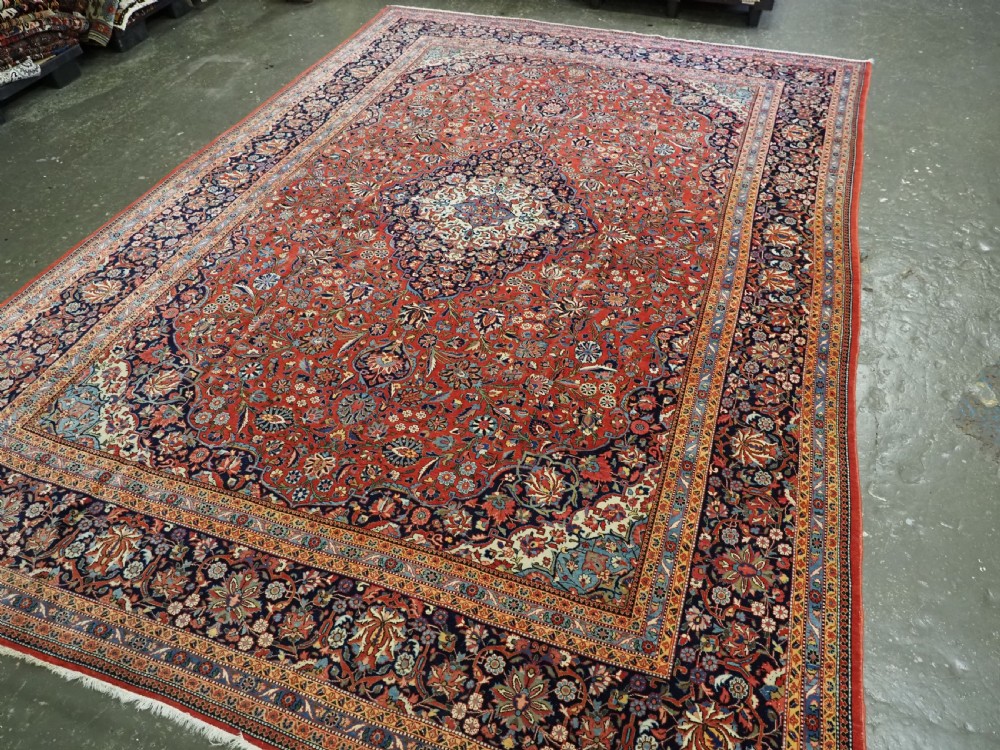 A large hand-knotted antique Kashan carpet featuring a central navy and ivory medallion on a crimson field with intricate floral patterns and layered borders. View III