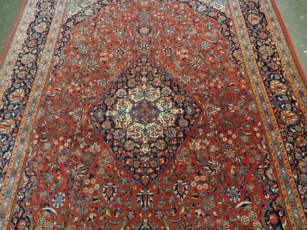 A large hand-knotted antique Kashan carpet featuring a central navy and ivory medallion on a crimson field with intricate floral patterns and layered borders. View IV