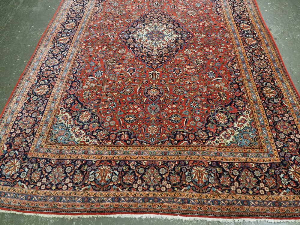A large hand-knotted antique Kashan carpet featuring a central navy and ivory medallion on a crimson field with intricate floral patterns and layered borders. View V