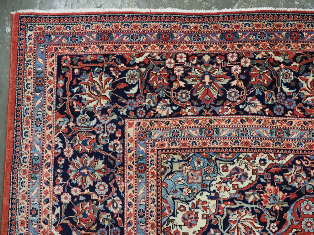 A large hand-knotted antique Kashan carpet featuring a central navy and ivory medallion on a crimson field with intricate floral patterns and layered borders. View VI