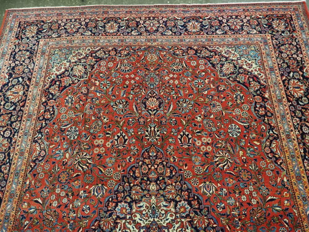 A large hand-knotted antique Kashan carpet featuring a central navy and ivory medallion on a crimson field with intricate floral patterns and layered borders. View VII