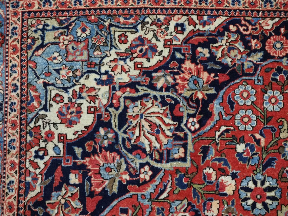 A large hand-knotted antique Kashan carpet featuring a central navy and ivory medallion on a crimson field with intricate floral patterns and layered borders. View IX