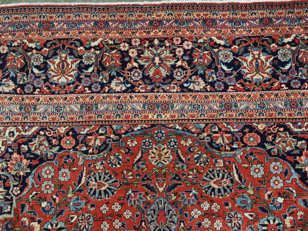 A large hand-knotted antique Kashan carpet featuring a central navy and ivory medallion on a crimson field with intricate floral patterns and layered borders. View X