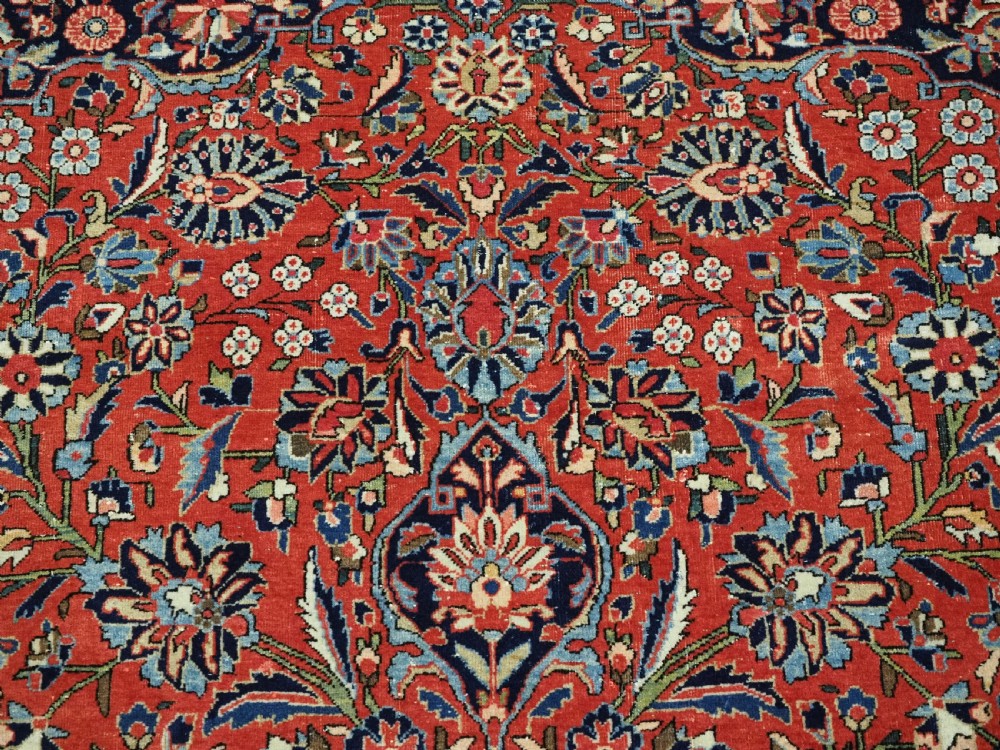 A large hand-knotted antique Kashan carpet featuring a central navy and ivory medallion on a crimson field with intricate floral patterns and layered borders. View XI