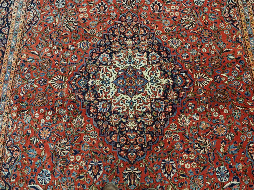 A large hand-knotted antique Kashan carpet featuring a central navy and ivory medallion on a crimson field with intricate floral patterns and layered borders. View XII