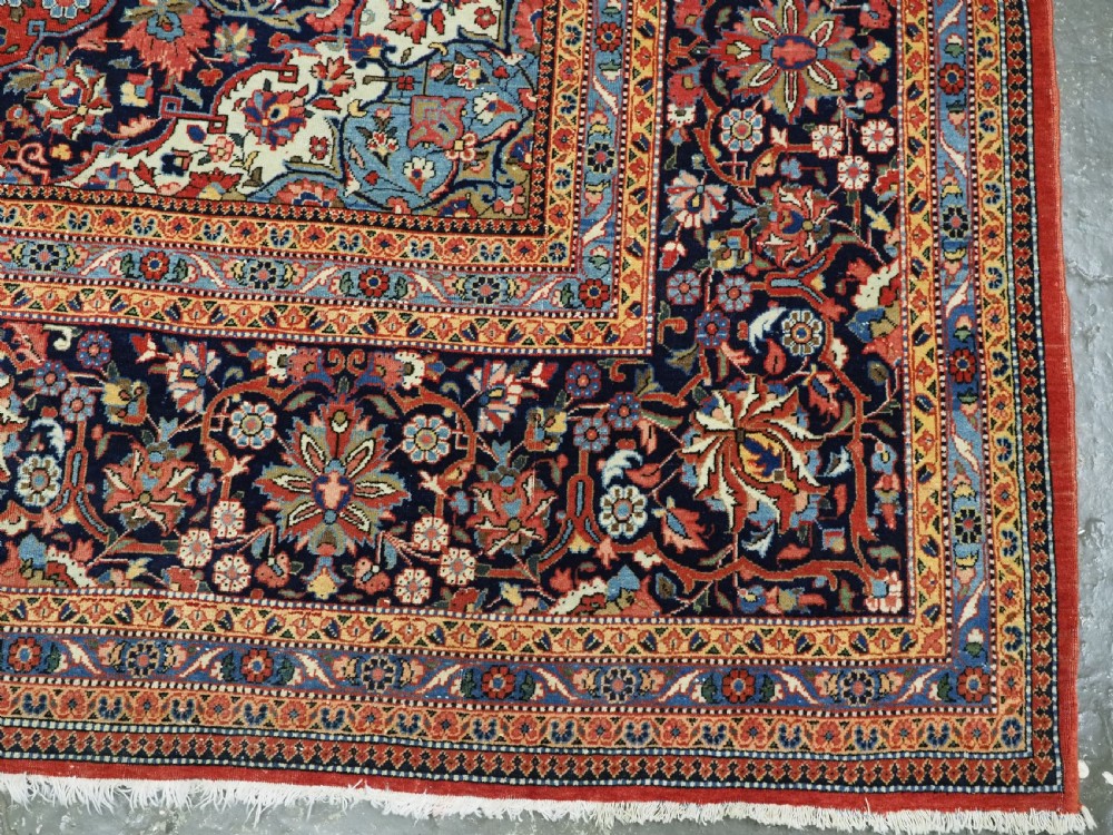 A large hand-knotted antique Kashan carpet featuring a central navy and ivory medallion on a crimson field with intricate floral patterns and layered borders. View XVIII
