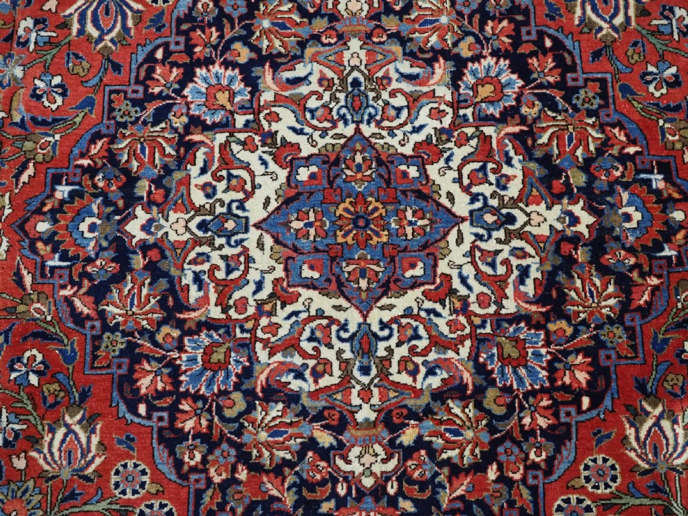A large hand-knotted antique Kashan carpet featuring a central navy and ivory medallion on a crimson field with intricate floral patterns and layered borders. View XIX