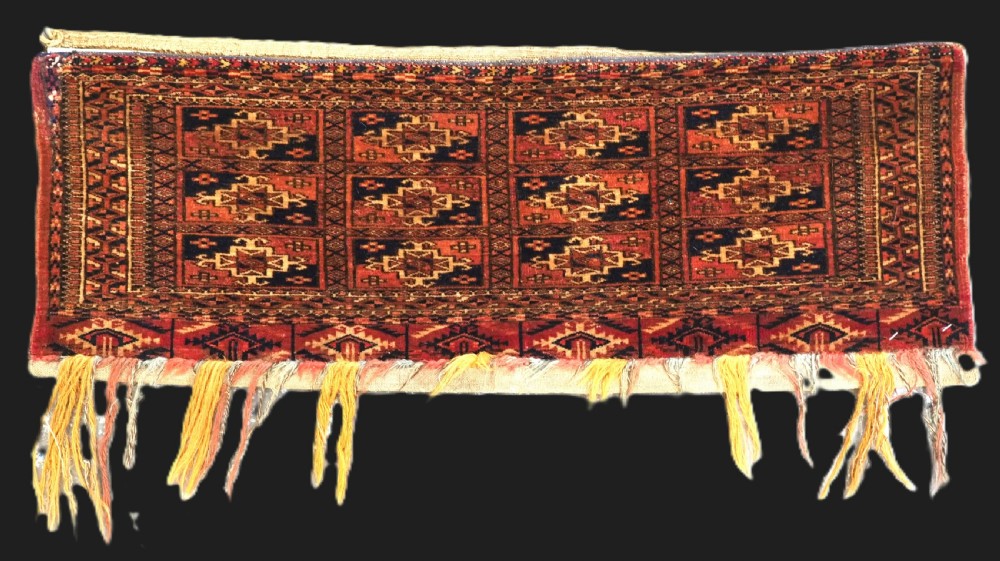 A rectangular Tekke Turkmen woven wool torba bag featuring repeating geometric gul motifs in red, navy, and ivory with a fringed bottom edge.