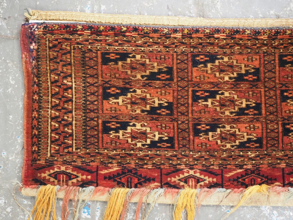 A rectangular Tekke Turkmen woven wool torba bag featuring repeating geometric gul motifs in red, navy, and ivory with a fringed bottom edge. View II
