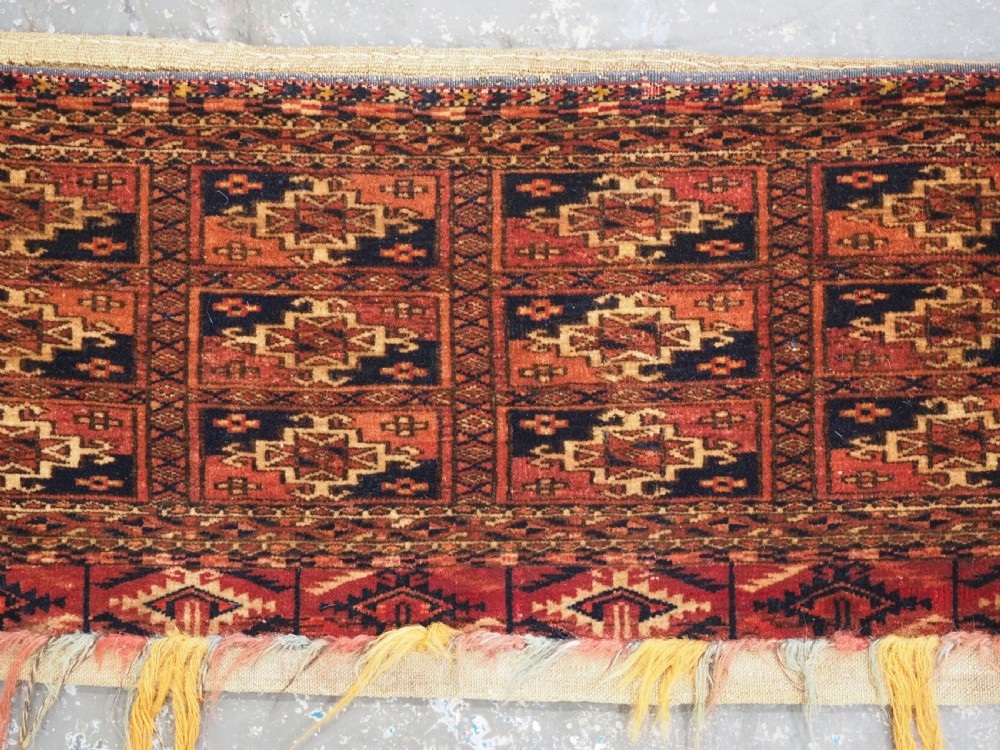 A rectangular Tekke Turkmen woven wool torba bag featuring repeating geometric gul motifs in red, navy, and ivory with a fringed bottom edge. View III