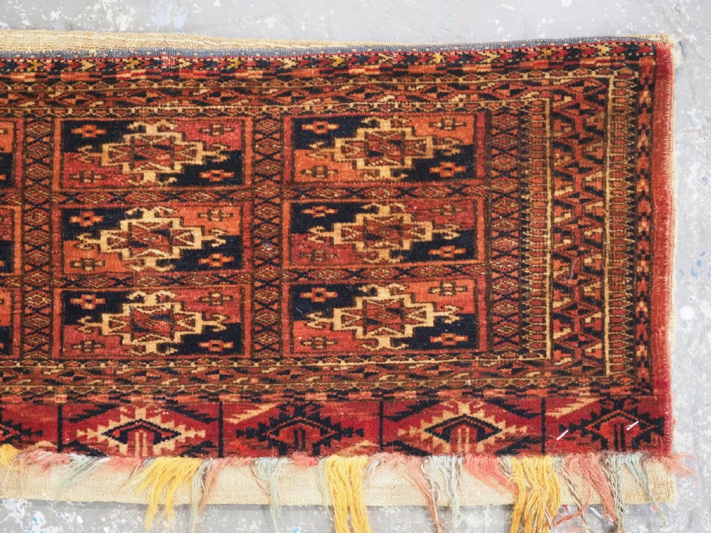 A rectangular Tekke Turkmen woven wool torba bag featuring repeating geometric gul motifs in red, navy, and ivory with a fringed bottom edge. View IV