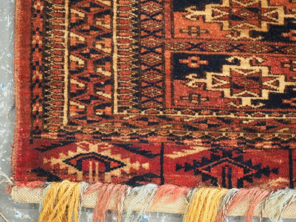 A rectangular Tekke Turkmen woven wool torba bag featuring repeating geometric gul motifs in red, navy, and ivory with a fringed bottom edge. View V