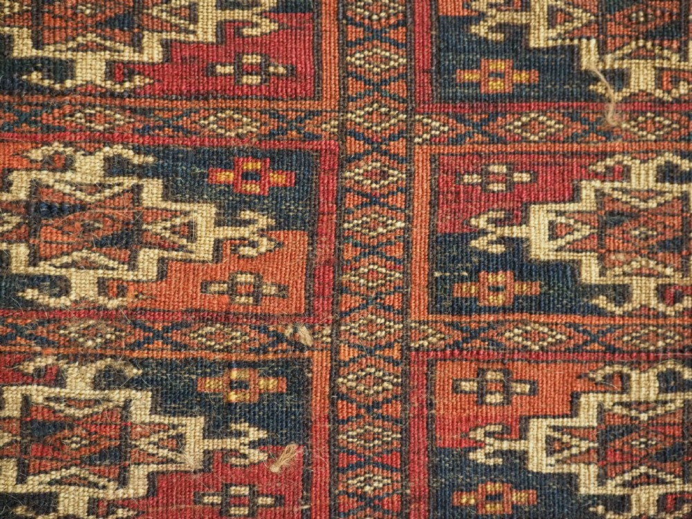 A rectangular Tekke Turkmen woven wool torba bag featuring repeating geometric gul motifs in red, navy, and ivory with a fringed bottom edge. View X