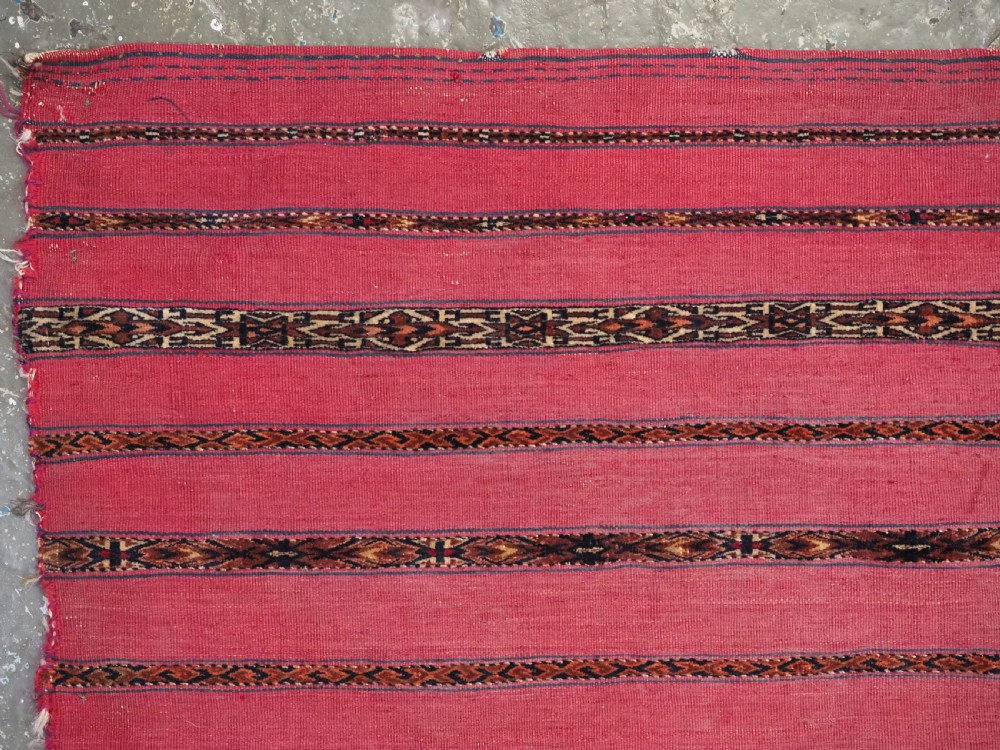 A rectangular red woven Turkmen Tekke chuval face featuring horizontal bands of geometric motifs. View III