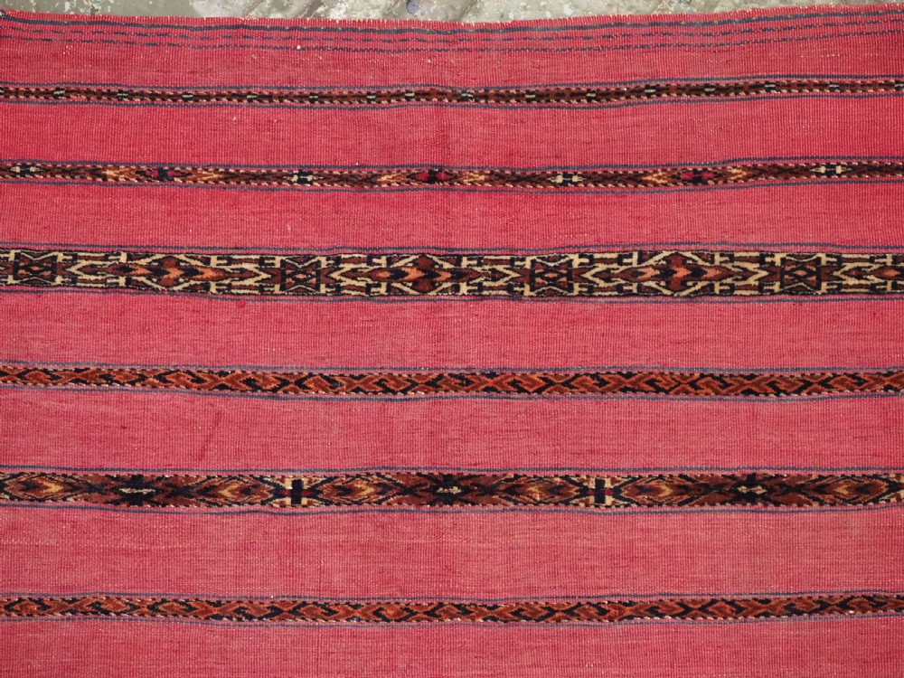 A rectangular red woven Turkmen Tekke chuval face featuring horizontal bands of geometric motifs. View V