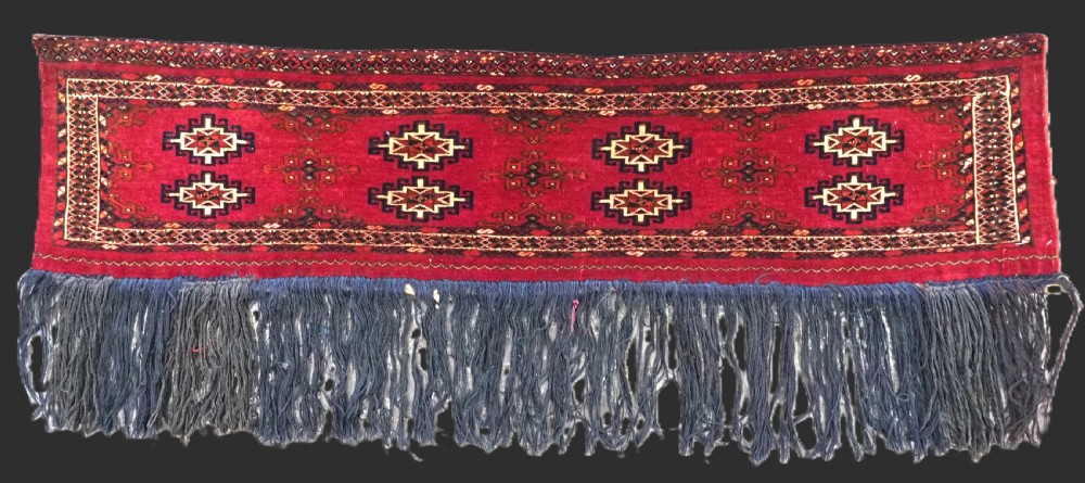 A horizontal crimson red Saryk Turkmen torba textile featuring octagonal Salor guls, intricate geometric borders, and a long dark lower fringe.