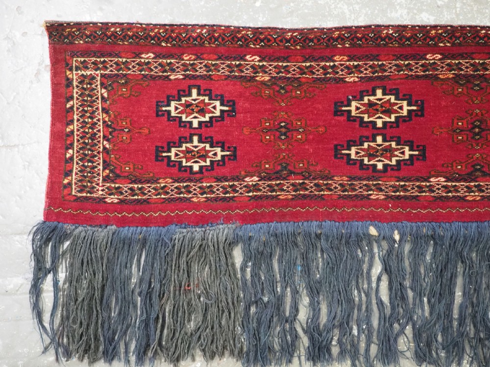 A horizontal crimson red Saryk Turkmen torba textile featuring octagonal Salor guls, intricate geometric borders, and a long dark lower fringe. View II