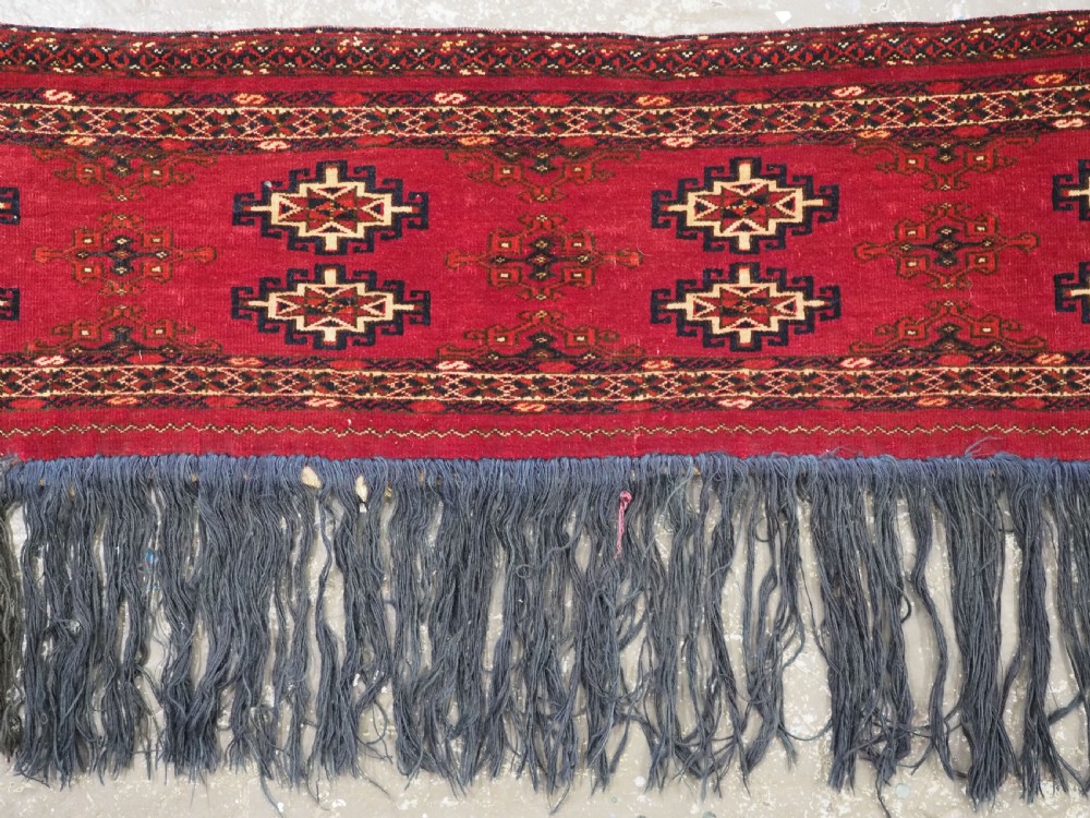 A horizontal crimson red Saryk Turkmen torba textile featuring octagonal Salor guls, intricate geometric borders, and a long dark lower fringe. View III