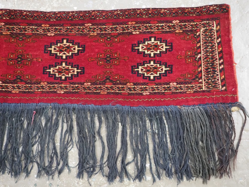 A horizontal crimson red Saryk Turkmen torba textile featuring octagonal Salor guls, intricate geometric borders, and a long dark lower fringe. View IV