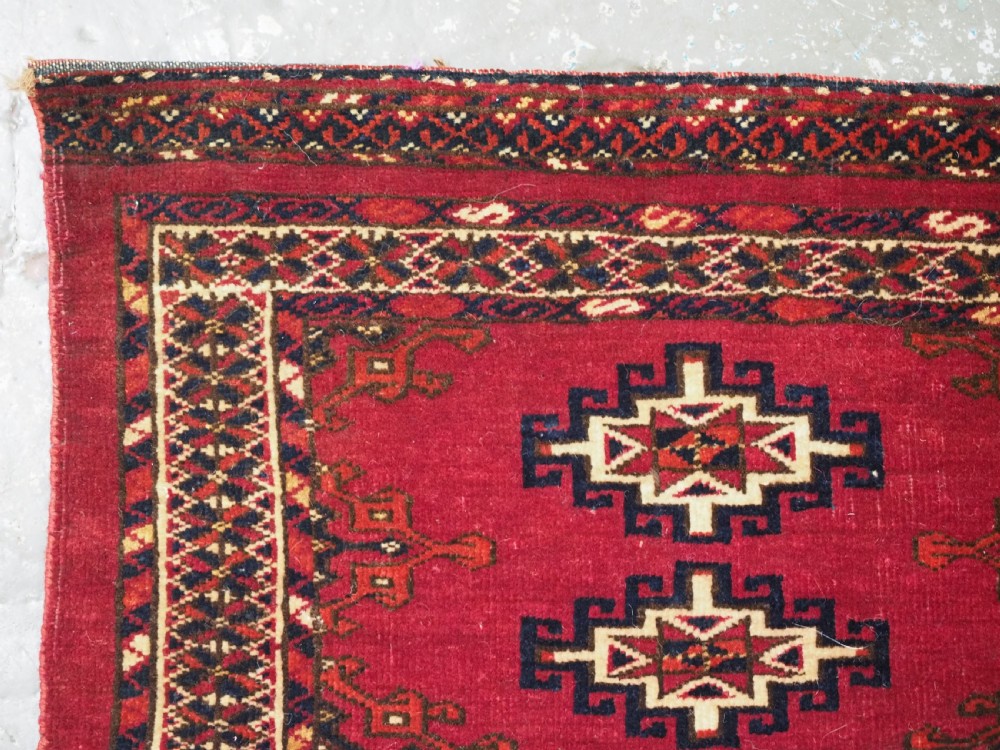A horizontal crimson red Saryk Turkmen torba textile featuring octagonal Salor guls, intricate geometric borders, and a long dark lower fringe. View V