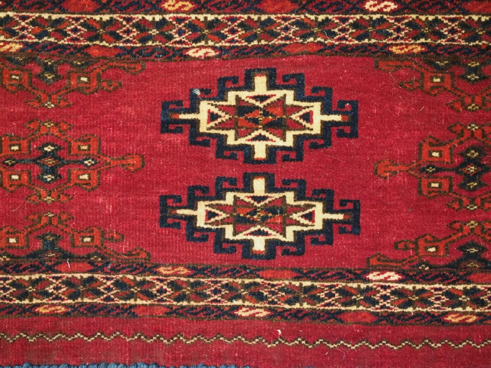 A horizontal crimson red Saryk Turkmen torba textile featuring octagonal Salor guls, intricate geometric borders, and a long dark lower fringe. View VI