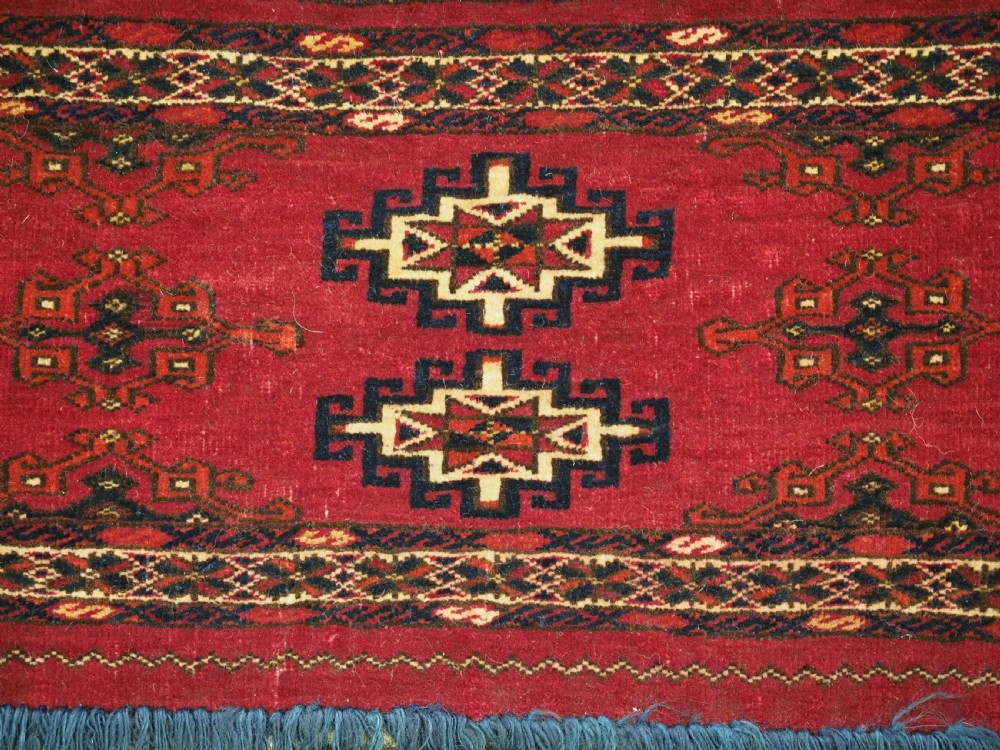 A horizontal crimson red Saryk Turkmen torba textile featuring octagonal Salor guls, intricate geometric borders, and a long dark lower fringe. View VII