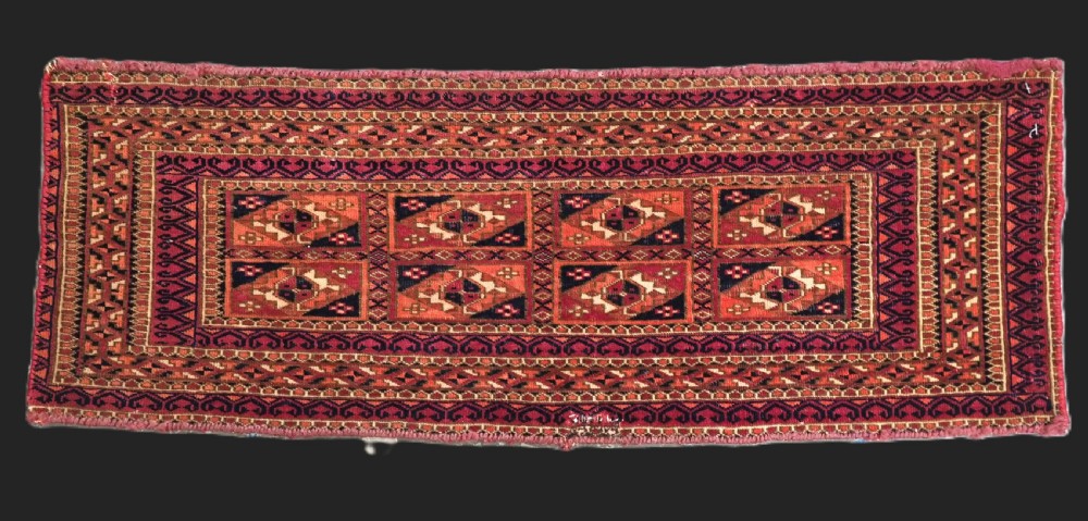 A rectangular hand-knotted wool textile panel featuring geometric Aina Gul motifs in shades of deep crimson, navy blue, and terracotta.