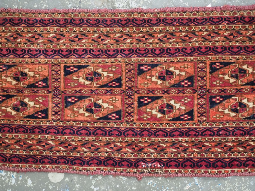 A rectangular hand-knotted wool textile panel featuring geometric Aina Gul motifs in shades of deep crimson, navy blue, and terracotta. View III