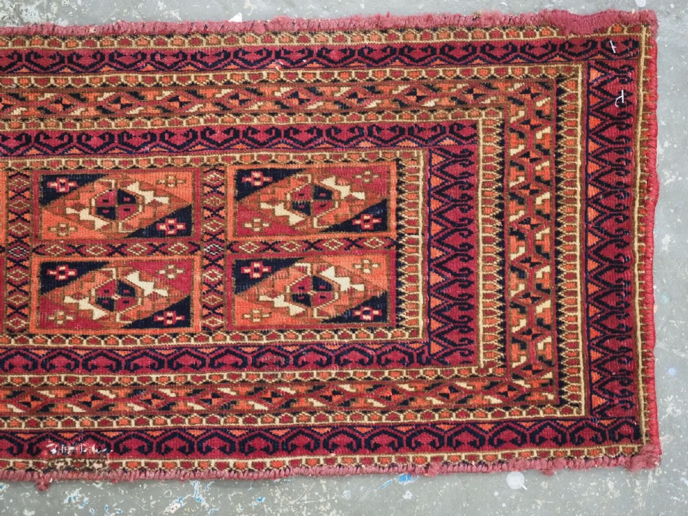 A rectangular hand-knotted wool textile panel featuring geometric Aina Gul motifs in shades of deep crimson, navy blue, and terracotta. View IV