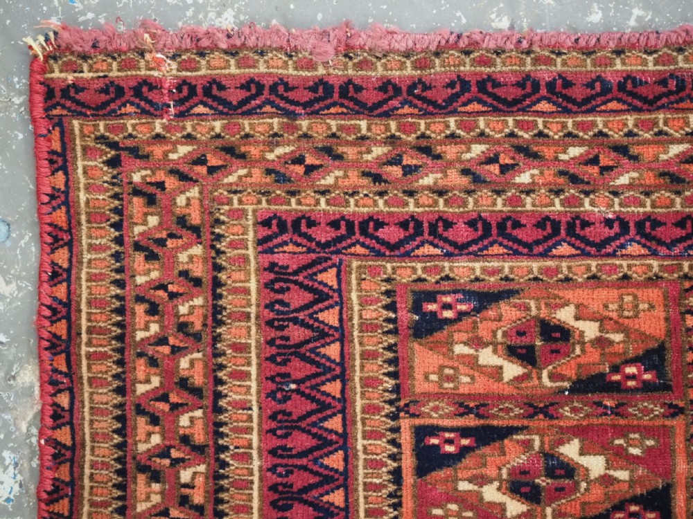 A rectangular hand-knotted wool textile panel featuring geometric Aina Gul motifs in shades of deep crimson, navy blue, and terracotta. View V