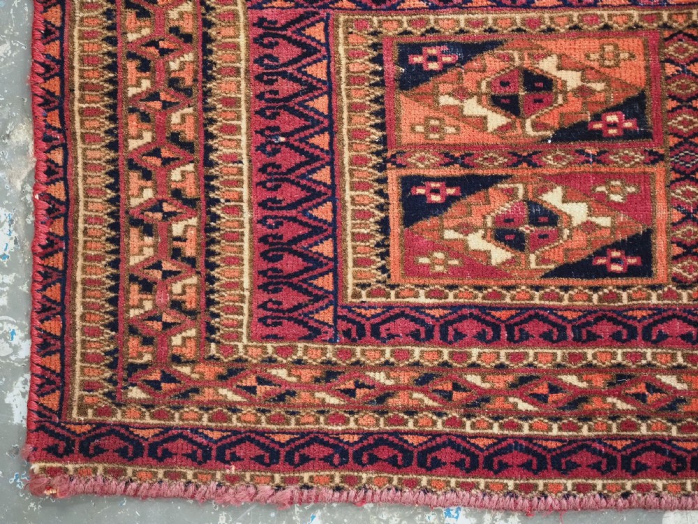 A rectangular hand-knotted wool textile panel featuring geometric Aina Gul motifs in shades of deep crimson, navy blue, and terracotta. View VI