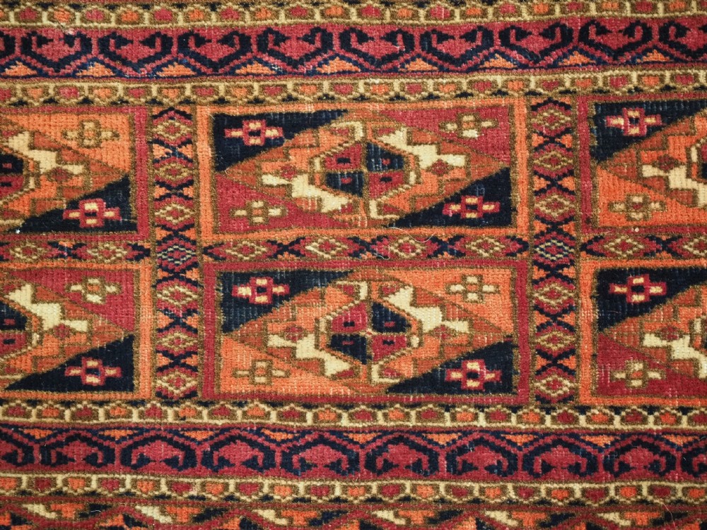 A rectangular hand-knotted wool textile panel featuring geometric Aina Gul motifs in shades of deep crimson, navy blue, and terracotta. View VII