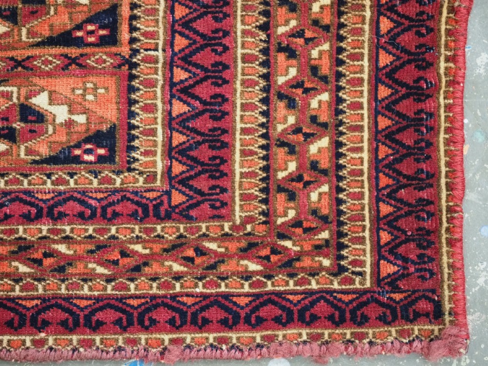 A rectangular hand-knotted wool textile panel featuring geometric Aina Gul motifs in shades of deep crimson, navy blue, and terracotta. View X