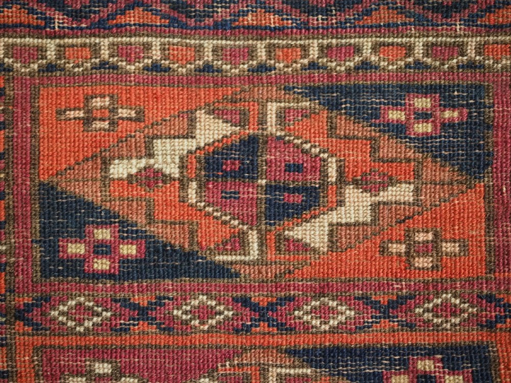 A rectangular hand-knotted wool textile panel featuring geometric Aina Gul motifs in shades of deep crimson, navy blue, and terracotta. View XI