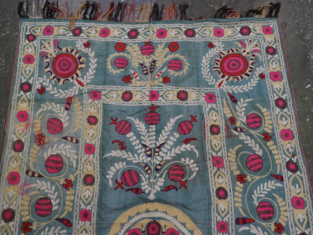 An antique teal silk suzani textile embroidered with pink and red pomegranate motifs, floral medallions, and decorative borders with top fringe. View III