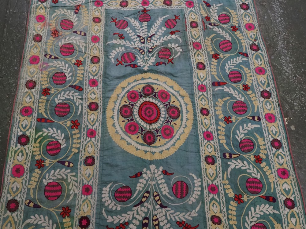 An antique teal silk suzani textile embroidered with pink and red pomegranate motifs, floral medallions, and decorative borders with top fringe. View IV