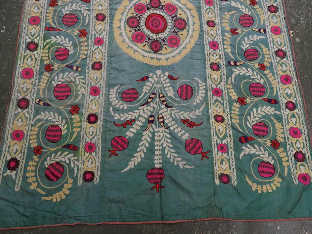 An antique teal silk suzani textile embroidered with pink and red pomegranate motifs, floral medallions, and decorative borders with top fringe. View V