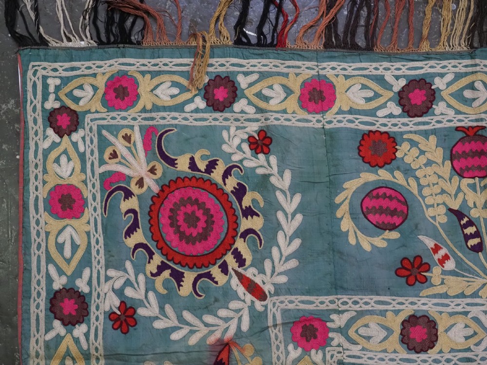 An antique teal silk suzani textile embroidered with pink and red pomegranate motifs, floral medallions, and decorative borders with top fringe. View VI