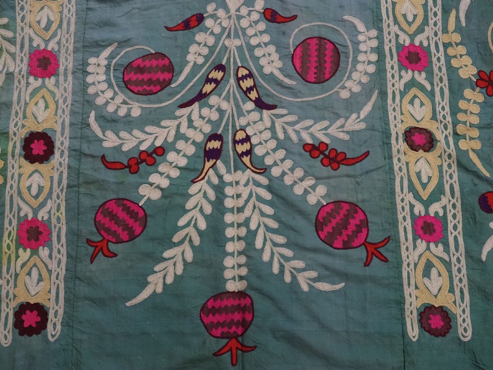 An antique teal silk suzani textile embroidered with pink and red pomegranate motifs, floral medallions, and decorative borders with top fringe. View IX