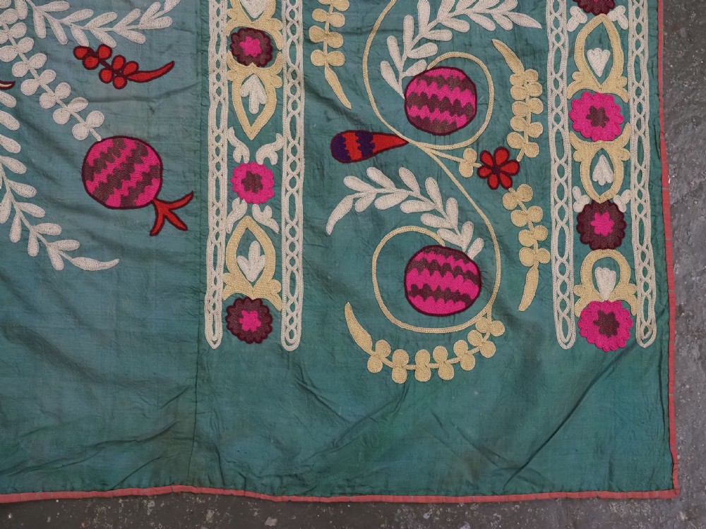 An antique teal silk suzani textile embroidered with pink and red pomegranate motifs, floral medallions, and decorative borders with top fringe. View X