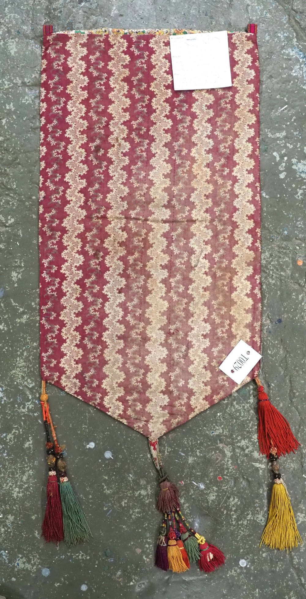 A shield-shaped Uzbek Lakai embroidered textile featuring vibrant silk floral and scroll motifs on a dark green background with long decorative tassels along the lower edge. View VIII