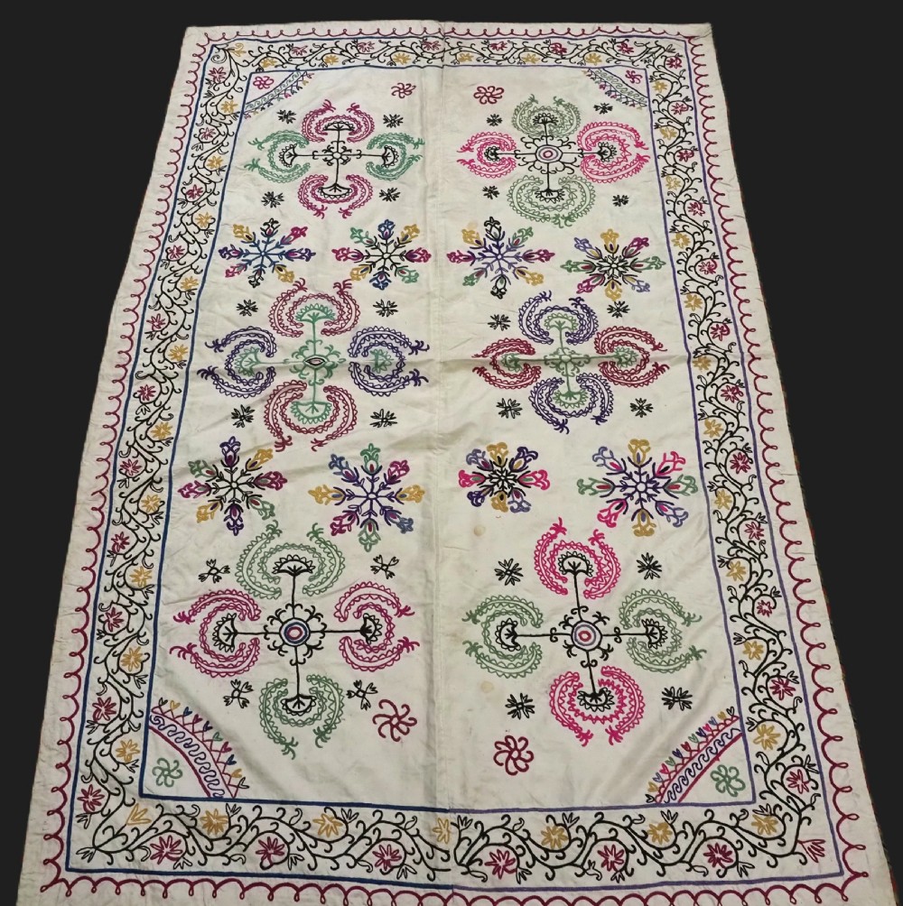 A rectangular antique cream silk Suzani textile featuring hand embroidery with multi-coloured floral roundels and vine borders.