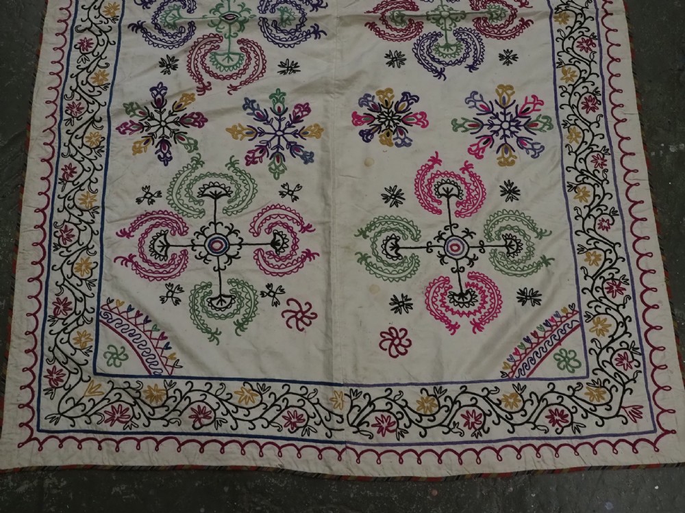 A rectangular antique cream silk Suzani textile featuring hand embroidery with multi-coloured floral roundels and vine borders. View V